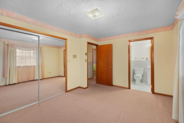 unfurnished bedroom with carpet flooring, ensuite bath, a textured ceiling, baseboards, and a closet