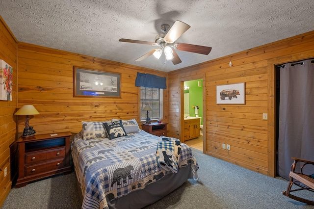 bedroom with ceiling fan, connected bathroom, a textured ceiling, and dark carpet