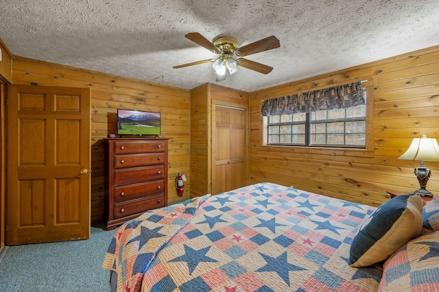 carpeted bedroom with ceiling fan, a closet, a textured ceiling, and wood walls
