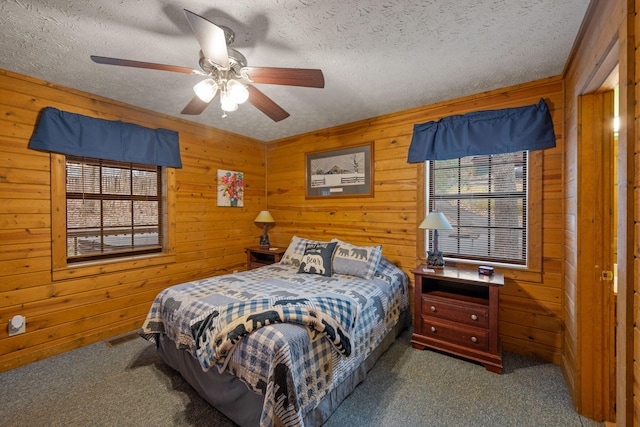 bedroom featuring ceiling fan, dark carpet, a textured ceiling, and wood walls