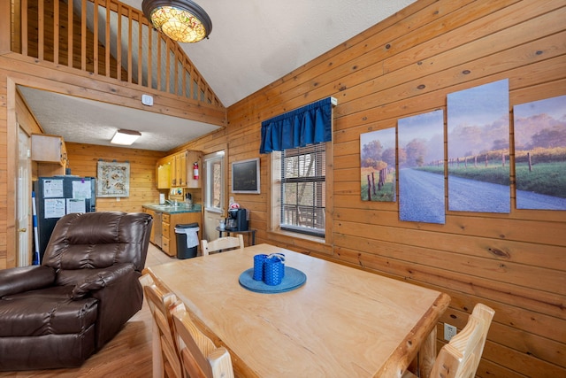 dining area with light hardwood / wood-style flooring, high vaulted ceiling, and wood walls
