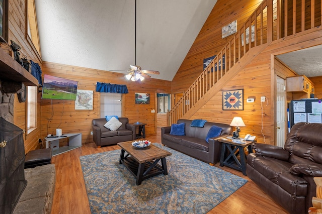living room featuring wood-type flooring, high vaulted ceiling, ceiling fan, and wood walls