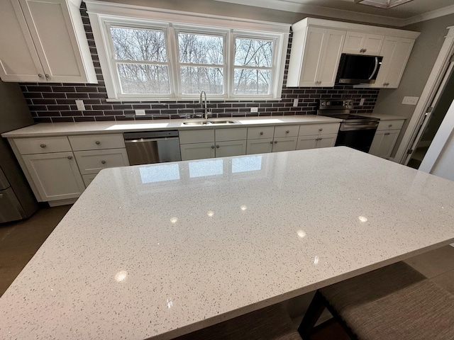 kitchen with light stone counters, stainless steel appliances, backsplash, white cabinetry, and a sink