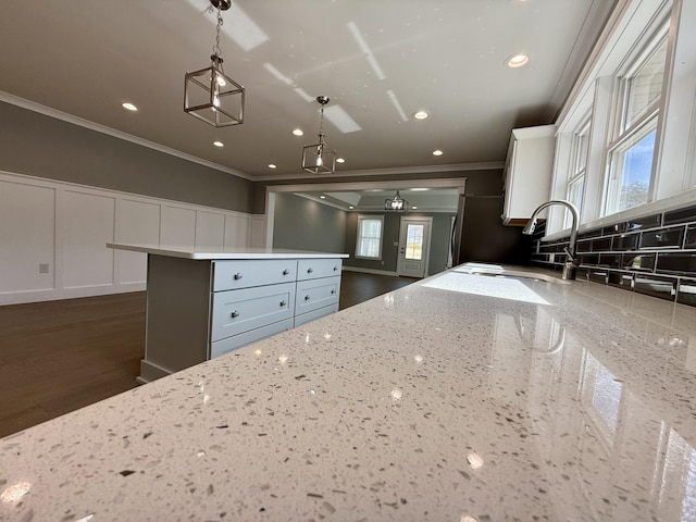 kitchen featuring light stone counters, a decorative wall, ornamental molding, white cabinets, and a sink