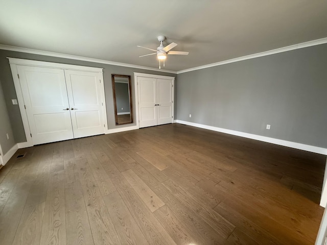 unfurnished bedroom with ceiling fan, baseboards, multiple closets, ornamental molding, and dark wood-style floors