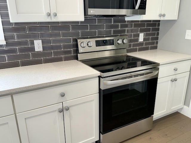 kitchen with appliances with stainless steel finishes, white cabinets, light wood-style floors, and backsplash