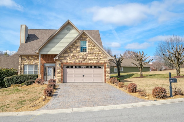 view of front facade featuring decorative driveway, stone siding, a front yard, a shingled roof, and a chimney