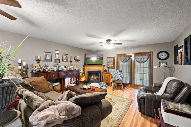 living room featuring light wood-type flooring, a lit fireplace, a textured ceiling, and ceiling fan