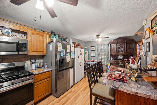 kitchen with light wood finished floors, decorative backsplash, a textured ceiling, appliances with stainless steel finishes, and ceiling fan
