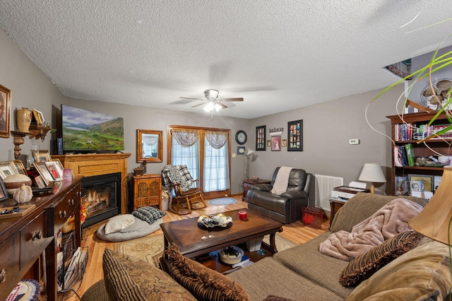 living area with wood finished floors, visible vents, a glass covered fireplace, a textured ceiling, and ceiling fan