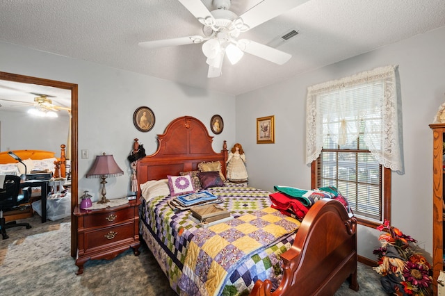 bedroom with a textured ceiling, dark colored carpet, visible vents, and ceiling fan