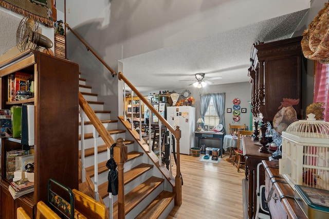 staircase with a ceiling fan, wood finished floors, and a textured ceiling