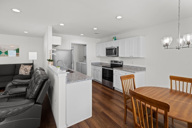 kitchen featuring stainless steel appliances, white cabinetry, washer and dryer, hanging light fixtures, and light stone countertops