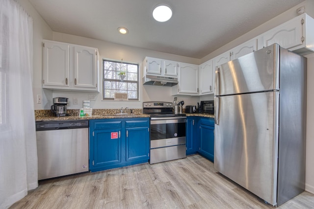 kitchen featuring blue cabinets, under cabinet range hood, light wood-style floors, appliances with stainless steel finishes, and white cabinets