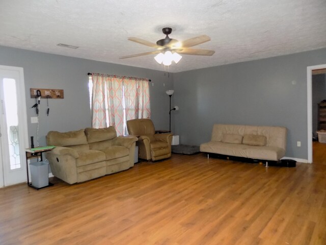 living room featuring ceiling fan, light wood-type flooring, and a textured ceiling