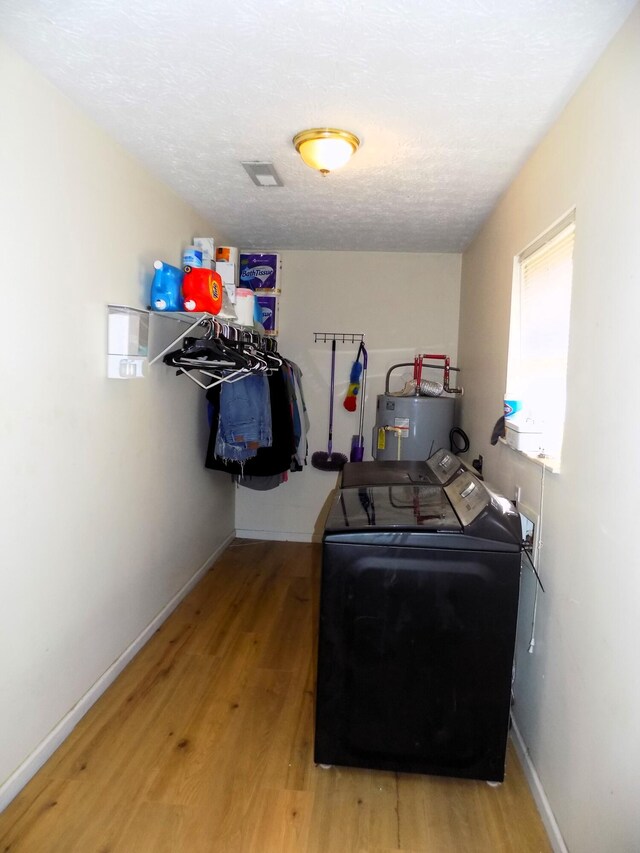 laundry area with hardwood / wood-style floors, washing machine and dryer, a textured ceiling, and water heater