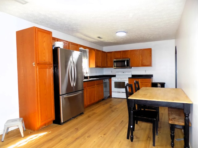 kitchen featuring sink, stainless steel appliances, a textured ceiling, and light wood-type flooring