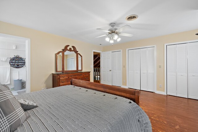 bedroom with ensuite bathroom, wood finished floors, visible vents, baseboards, and two closets