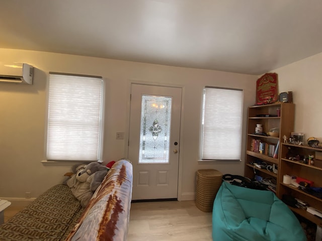 foyer entrance with a wall unit AC, light wood-type flooring, and baseboards