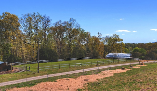 view of yard featuring a rural view, fence, a view of trees, and an outdoor structure