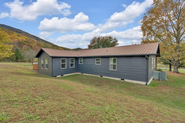 rear view of house with central air condition unit, a mountain view, and a lawn