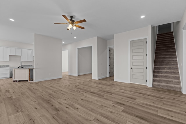 unfurnished living room featuring light wood-style flooring, baseboards, stairs, ceiling fan, and recessed lighting