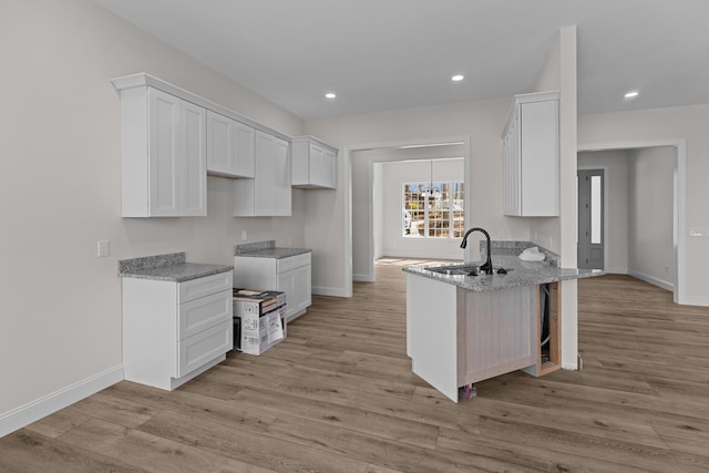 kitchen with white cabinetry, a sink, a peninsula, and light stone counters