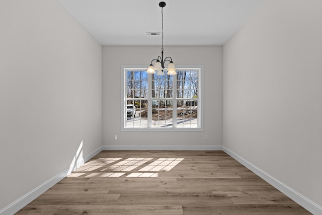 unfurnished dining area with baseboards, visible vents, wood finished floors, and a chandelier
