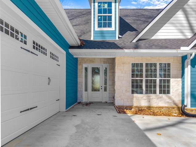 view of exterior entry featuring stone siding, driveway, and roof with shingles