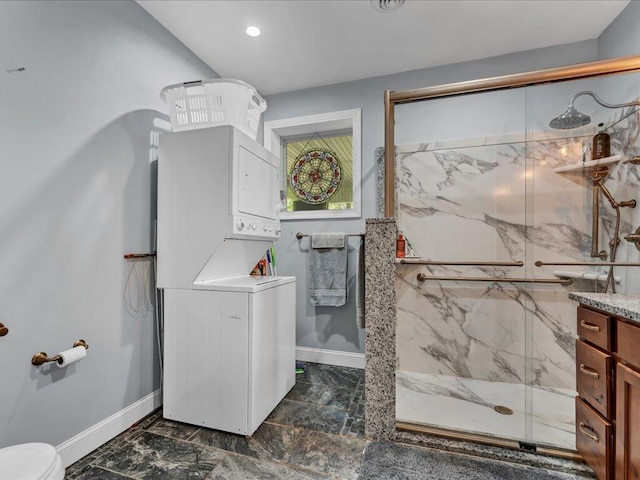 bathroom featuring stacked washer and dryer, vanity, a shower with door, and toilet