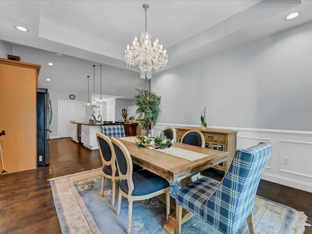 dining area with a raised ceiling, a notable chandelier, and dark hardwood / wood-style flooring