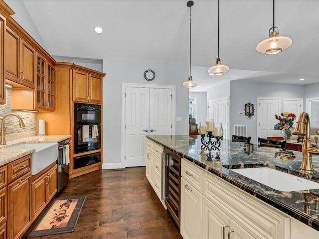 kitchen featuring pendant lighting, stainless steel dishwasher, sink, and dark stone counters