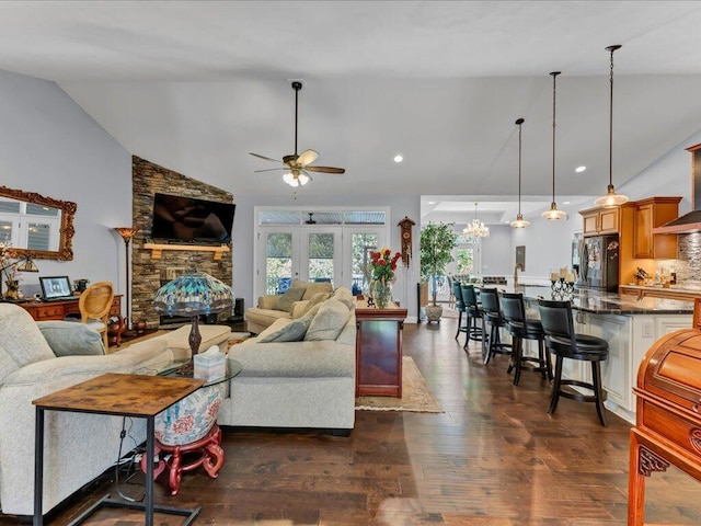 living room with french doors, dark hardwood / wood-style flooring, vaulted ceiling, ceiling fan, and a stone fireplace