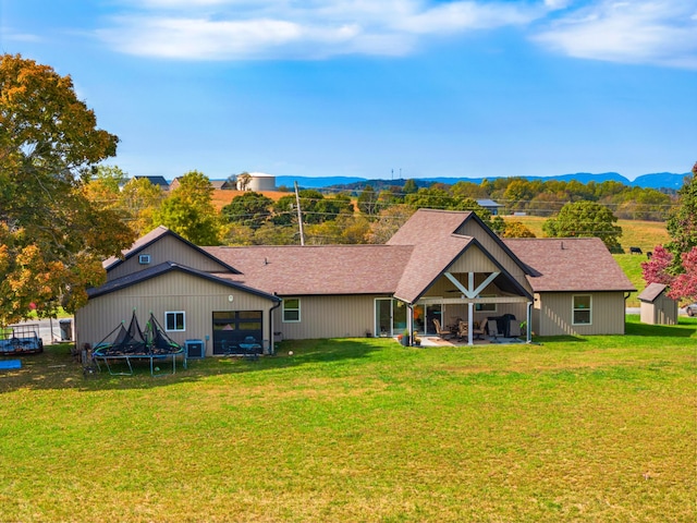 rear view of house with a lawn, central AC, a mountain view, and a trampoline