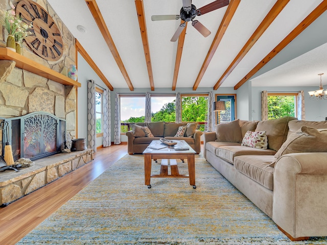 living room with wood finished floors, a stone fireplace, a ceiling fan, and a chandelier