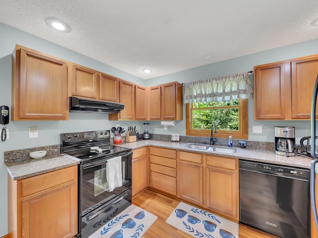 kitchen featuring black appliances, under cabinet range hood, a sink, light wood-style floors, and light stone counters