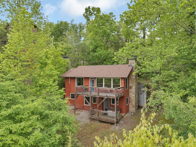 rear view of house featuring a wooden deck, a chimney, and roof with shingles