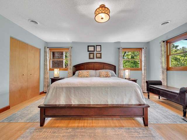 bedroom with multiple windows, a textured ceiling, wood finished floors, and a closet