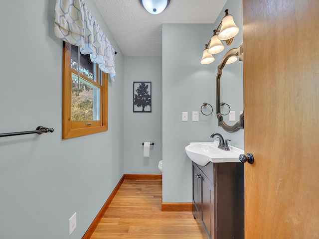 bathroom with wood finished floors, vanity, baseboards, a textured ceiling, and toilet