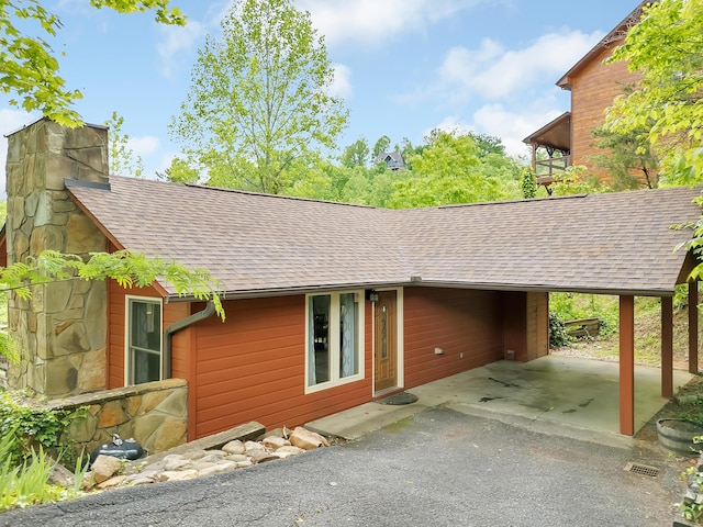view of side of property with a shingled roof, an attached carport, asphalt driveway, and a chimney