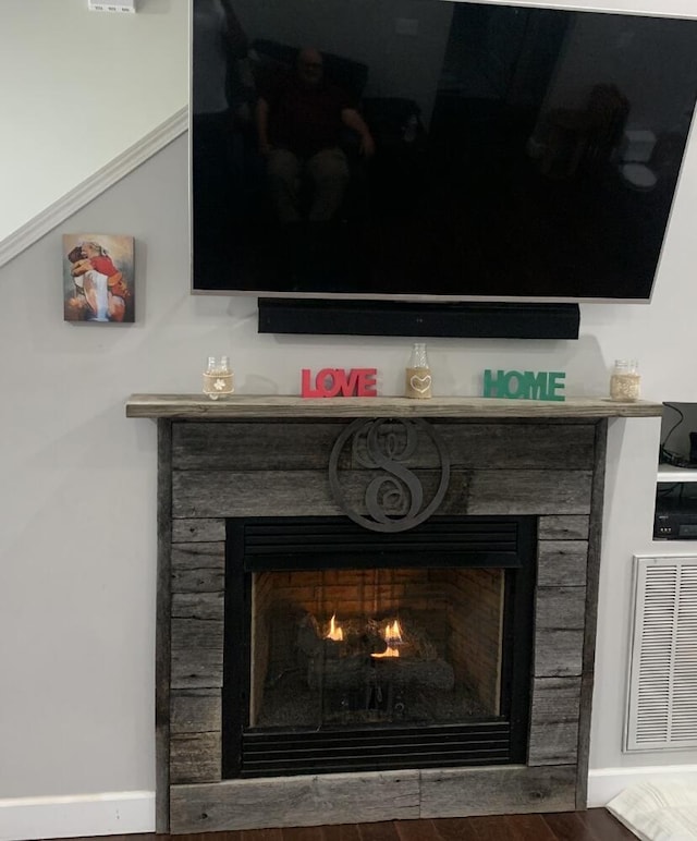 interior details with a warm lit fireplace, visible vents, and wood finished floors