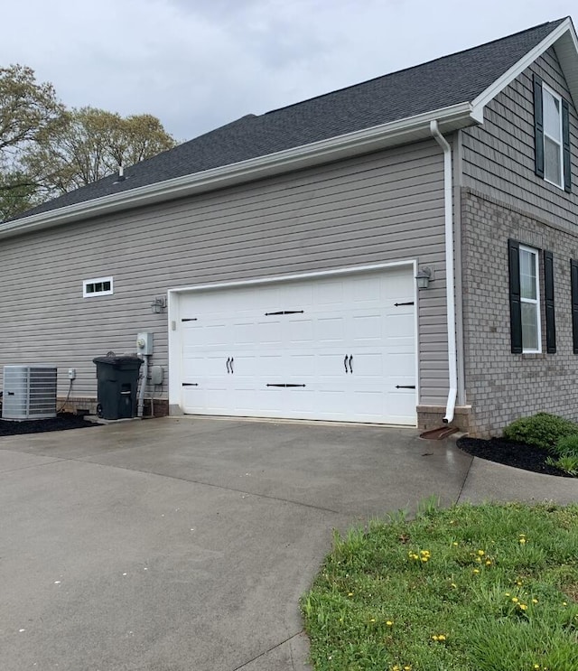 view of side of property featuring cooling unit, brick siding, driveway, and a garage