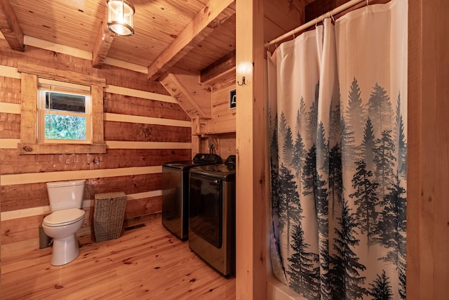 bathroom featuring wooden walls, beam ceiling, wooden ceiling, washing machine and dryer, and toilet