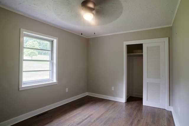 unfurnished bedroom with ceiling fan, dark hardwood / wood-style flooring, crown molding, a textured ceiling, and a closet