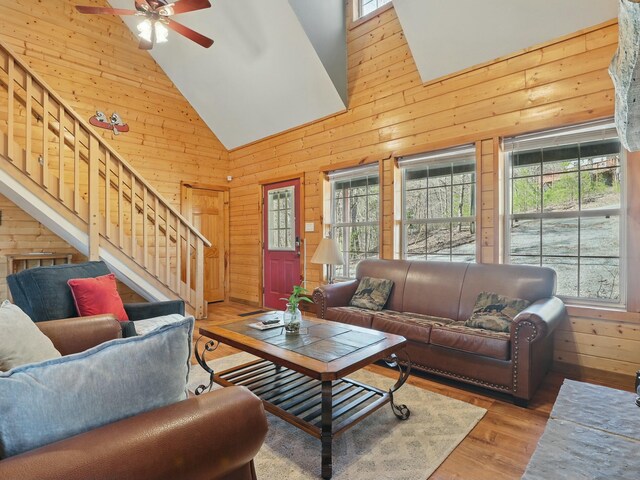 living room featuring stairs, a healthy amount of sunlight, wood walls, and ceiling fan
