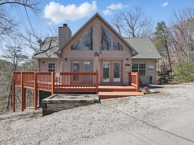 view of front of house with a chimney, a wooden deck, french doors, and a shingled roof