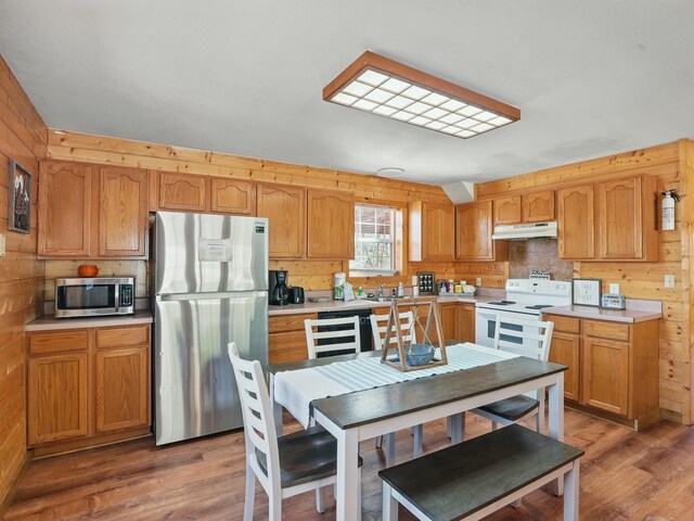 kitchen with under cabinet range hood, stainless steel appliances, wood finished floors, and light countertops