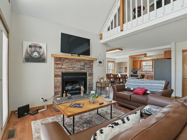 living area featuring visible vents, baseboards, a fireplace, a high ceiling, and wood finished floors