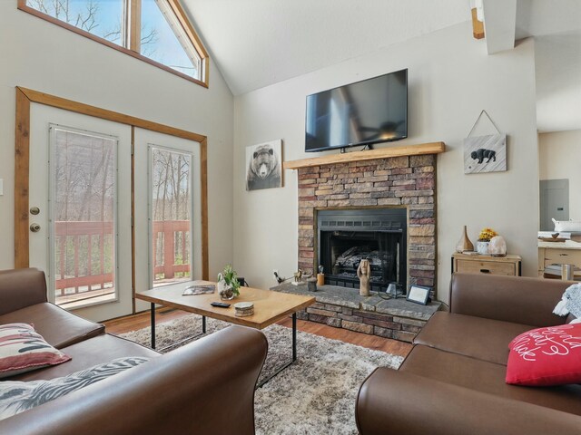 living room with a stone fireplace, electric panel, wood finished floors, and high vaulted ceiling