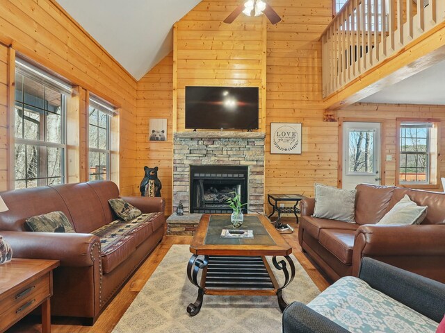 living room with wooden walls, wood finished floors, high vaulted ceiling, a fireplace, and ceiling fan